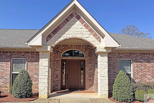 view of exterior entry featuring brick siding and a shingled roof