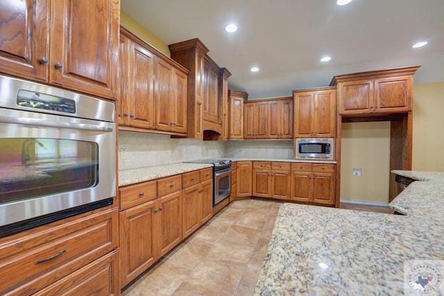 kitchen featuring light stone counters, decorative backsplash, brown cabinets, and appliances with stainless steel finishes