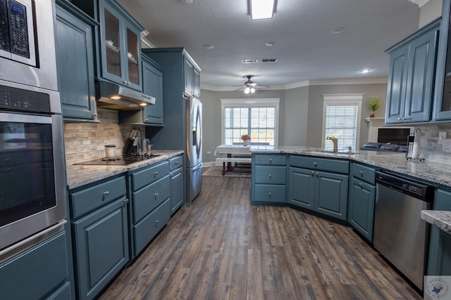 kitchen with blue cabinetry, appliances with stainless steel finishes, sink, backsplash, and light stone counters