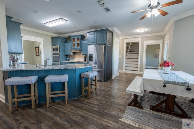 kitchen with appliances with stainless steel finishes, dark wood-type flooring, decorative backsplash, blue cabinetry, and crown molding