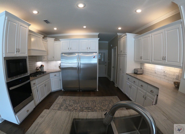 kitchen with custom range hood, white cabinetry, appliances with stainless steel finishes, and sink