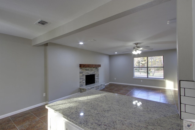 interior space featuring ceiling fan, light stone countertops, dark tile patterned floors, and a stone fireplace