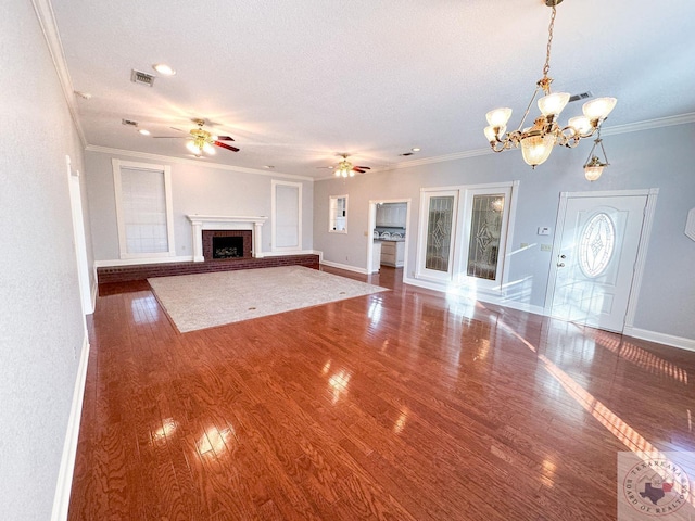 unfurnished living room with ceiling fan with notable chandelier, a brick fireplace, ornamental molding, and a textured ceiling