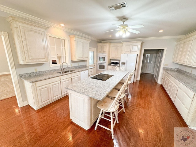 kitchen featuring white appliances, a kitchen island, sink, light stone counters, and a breakfast bar area