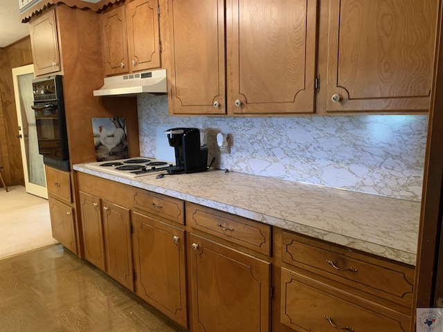 kitchen featuring brown cabinets, under cabinet range hood, black oven, white electric cooktop, and light countertops