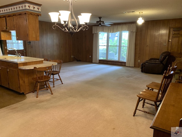 kitchen with sink, wood walls, hanging light fixtures, and light colored carpet