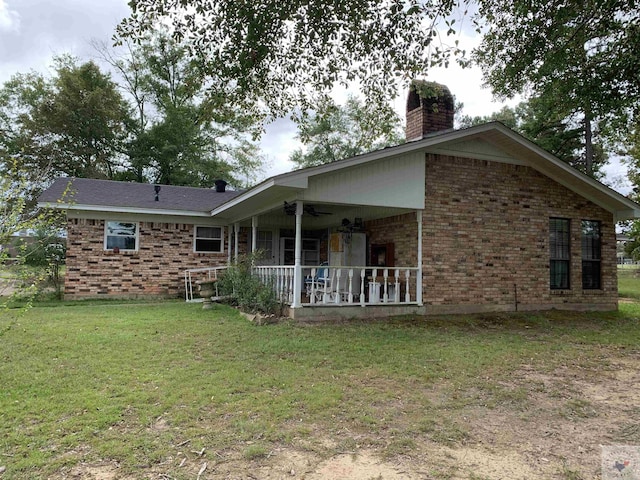 rear view of house with a ceiling fan, a yard, brick siding, a chimney, and a patio area