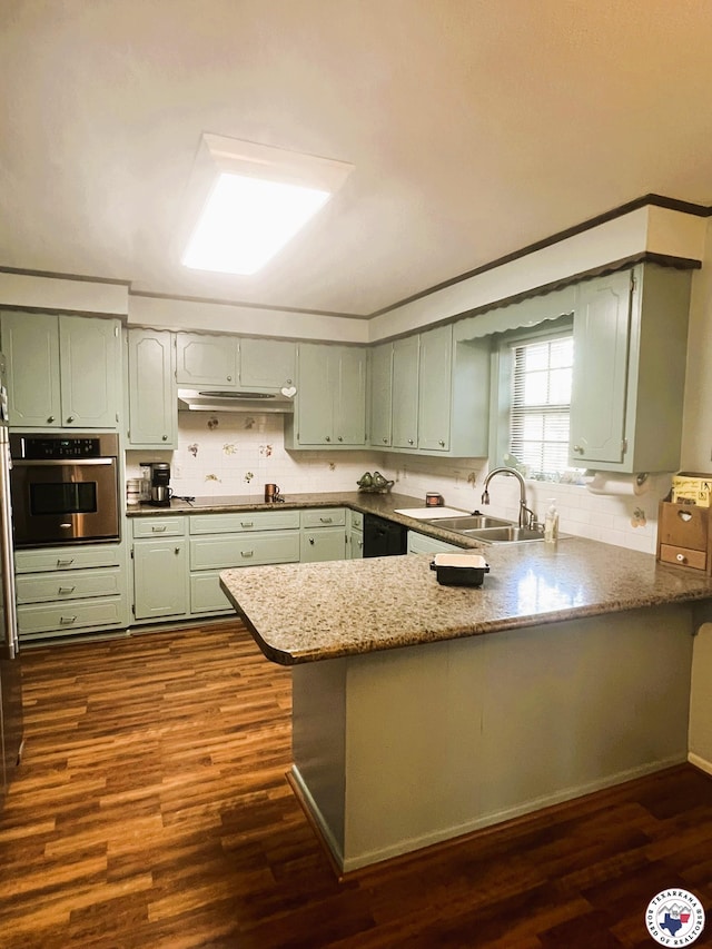 kitchen with dark wood finished floors, stainless steel oven, tasteful backsplash, a peninsula, and a sink