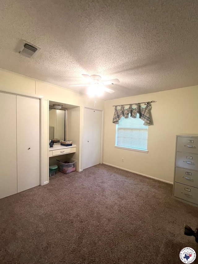 unfurnished bedroom featuring visible vents, ceiling fan, a textured ceiling, carpet floors, and multiple closets