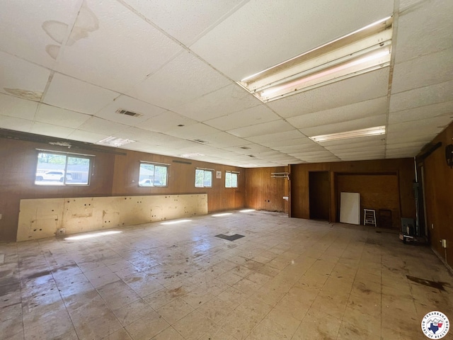 basement with visible vents, tile patterned floors, a drop ceiling, and wood walls