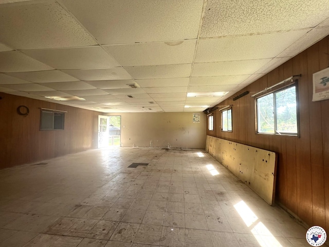 basement with wood walls, a drop ceiling, and plenty of natural light