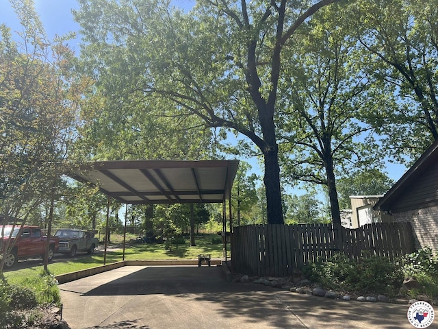 view of vehicle parking with driveway, a detached carport, and fence