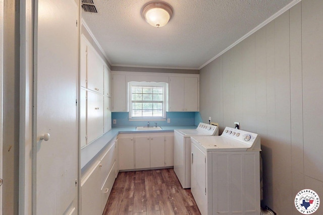 laundry area with cabinet space, independent washer and dryer, a sink, wood finished floors, and visible vents