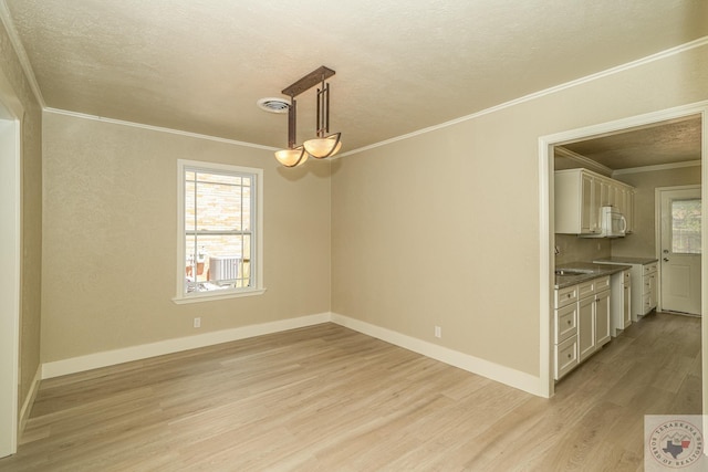 unfurnished dining area featuring light wood-type flooring, crown molding, and a textured ceiling