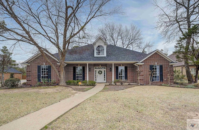 view of front facade with a front yard, brick siding, and roof with shingles