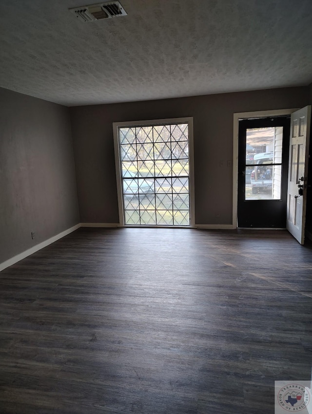 unfurnished room with a healthy amount of sunlight, a textured ceiling, and dark hardwood / wood-style floors