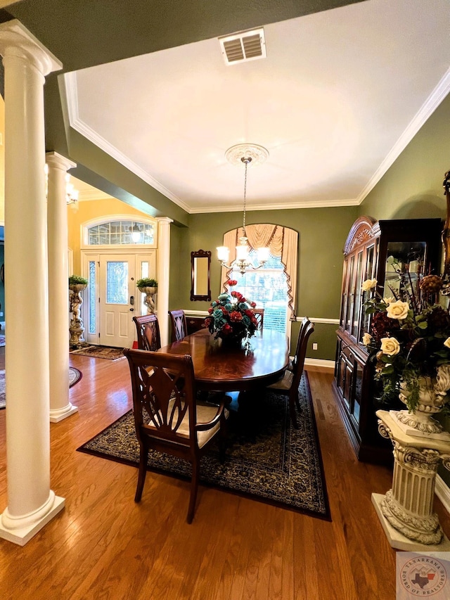 dining area featuring dark wood-type flooring, ornamental molding, and ornate columns