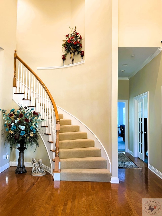 stairs featuring crown molding, hardwood / wood-style flooring, and a towering ceiling