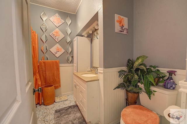 bathroom with a textured ceiling, tile patterned floors, vanity, toilet, and crown molding