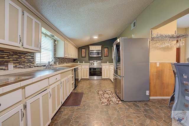 kitchen with white cabinets, appliances with stainless steel finishes, tile counters, lofted ceiling, and sink