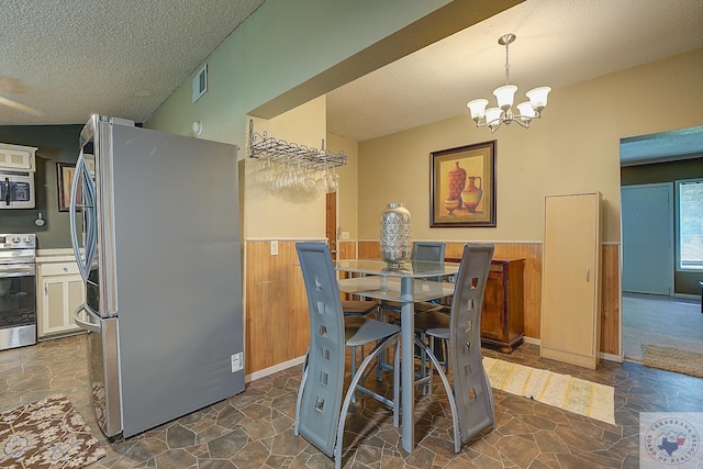 dining space with a textured ceiling, a chandelier, and wooden walls