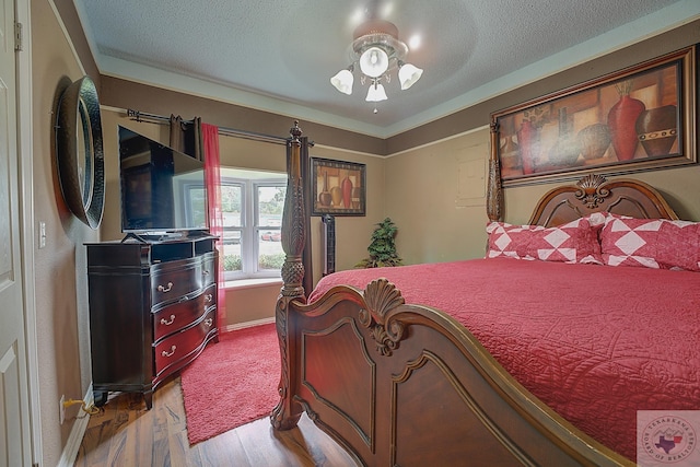 bedroom featuring light wood-type flooring, a textured ceiling, ceiling fan, and ornamental molding