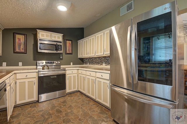 kitchen featuring a textured ceiling, appliances with stainless steel finishes, lofted ceiling, and tasteful backsplash