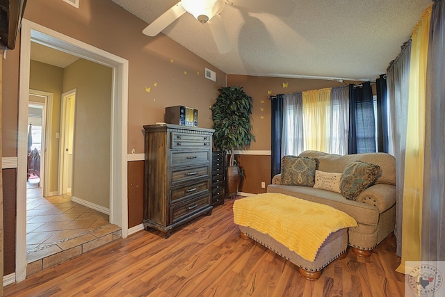 sitting room with vaulted ceiling, ceiling fan, light hardwood / wood-style floors, and a textured ceiling