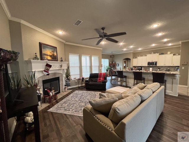 living room featuring ceiling fan, a tile fireplace, dark wood-type flooring, and crown molding