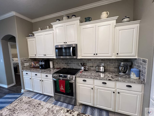 kitchen featuring ornamental molding, white cabinets, decorative backsplash, and appliances with stainless steel finishes