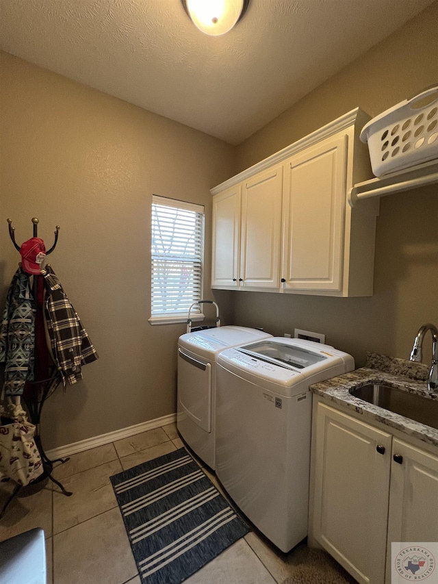 clothes washing area with sink, washer and clothes dryer, light tile patterned floors, and cabinets