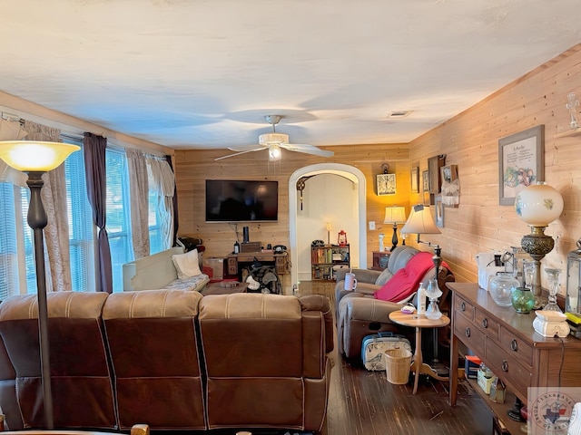 living room with ceiling fan, wood walls, and dark wood-type flooring