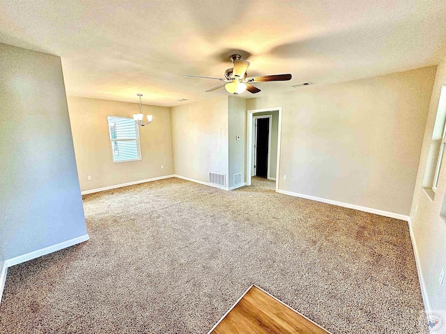 carpeted spare room featuring ceiling fan with notable chandelier and a textured ceiling