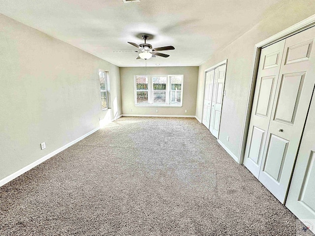 unfurnished bedroom featuring ceiling fan, multiple closets, and carpet flooring