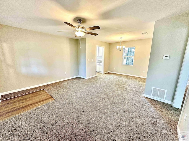 carpeted spare room featuring ceiling fan with notable chandelier and a textured ceiling