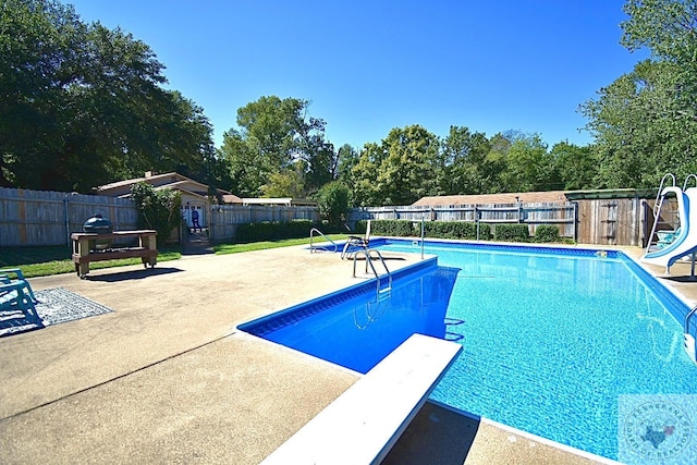 view of swimming pool with a water slide, a diving board, and a patio