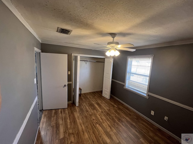 unfurnished bedroom featuring crown molding, a textured ceiling, dark hardwood / wood-style flooring, a closet, and ceiling fan