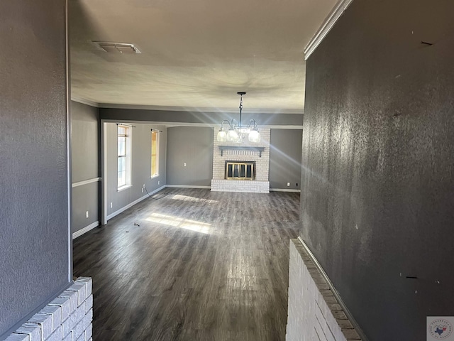 unfurnished living room with a fireplace, ornamental molding, dark hardwood / wood-style floors, and a chandelier