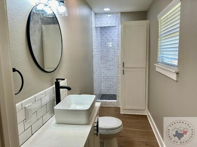 bathroom with hardwood / wood-style floors, tiled shower, toilet, and vanity