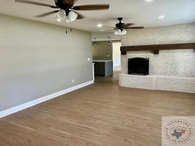 unfurnished living room with ceiling fan, hardwood / wood-style flooring, and a brick fireplace