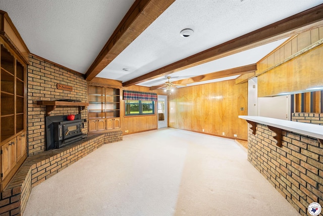 6514 Buchanan Loop, Texarkana, TX 75501 - unfurnished living room featuring a wood stove, wood walls, beam ceiling, ceiling fan, and a textured ceiling