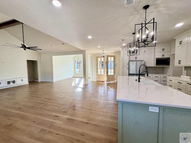 kitchen featuring light wood-style flooring, appliances with stainless steel finishes, a kitchen island with sink, white cabinetry, and backsplash