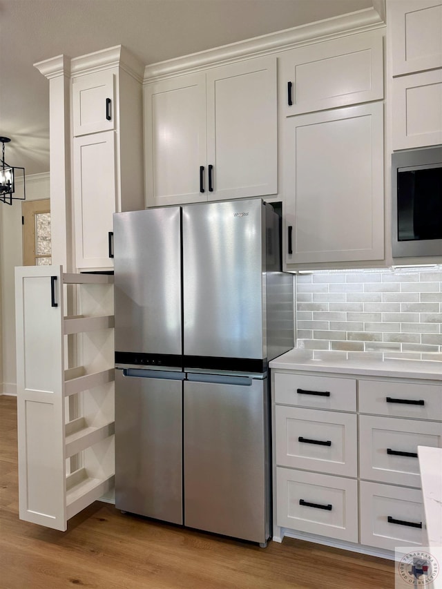 kitchen with crown molding, stainless steel appliances, tasteful backsplash, white cabinets, and light wood-type flooring