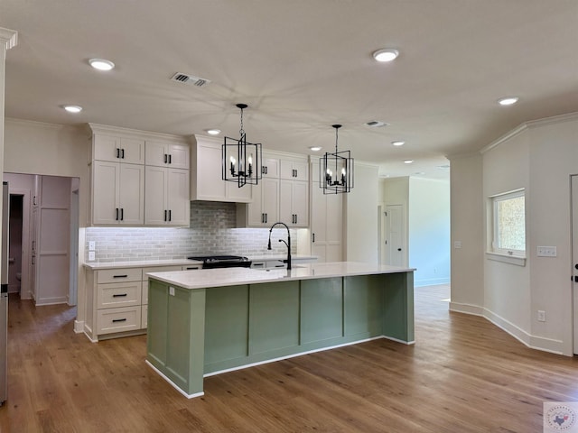 kitchen with ornamental molding, light countertops, an island with sink, and white cabinetry