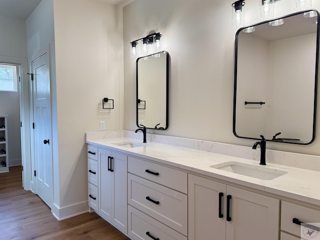 full bath with double vanity, wood finished floors, a sink, and baseboards