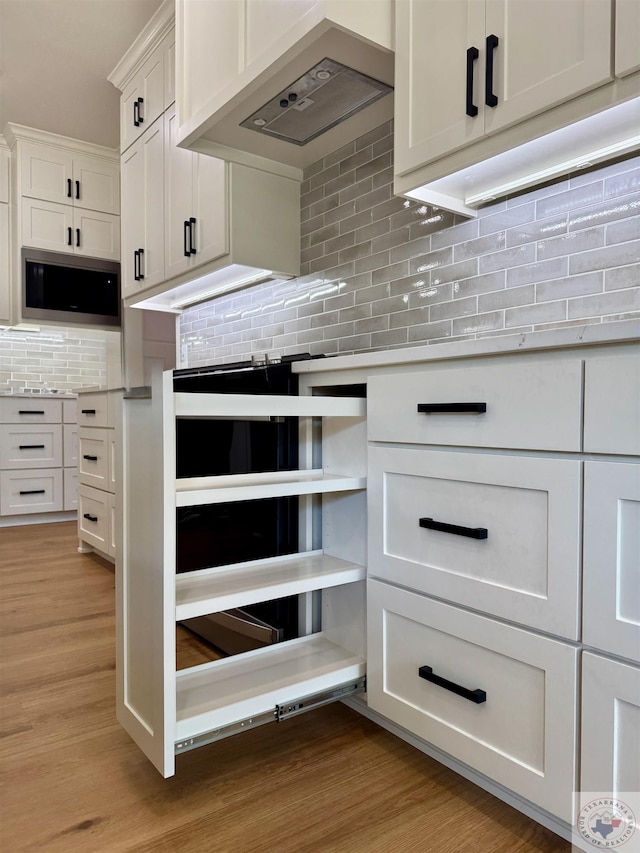 kitchen featuring tasteful backsplash, wine cooler, built in microwave, light countertops, and premium range hood