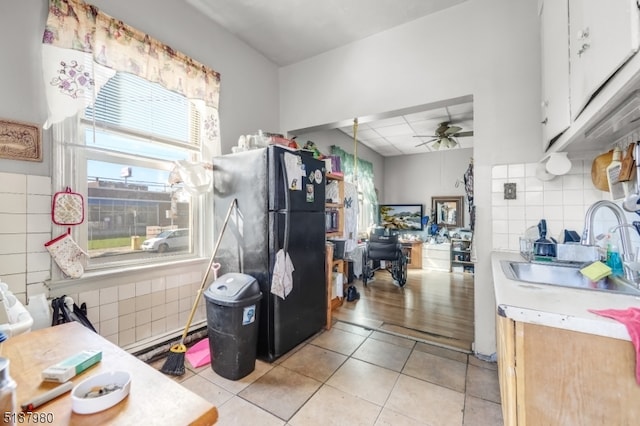 kitchen with ceiling fan, light tile floors, sink, white cabinetry, and black fridge