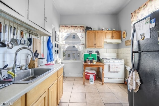 kitchen featuring backsplash, white gas stove, sink, light tile floors, and black fridge