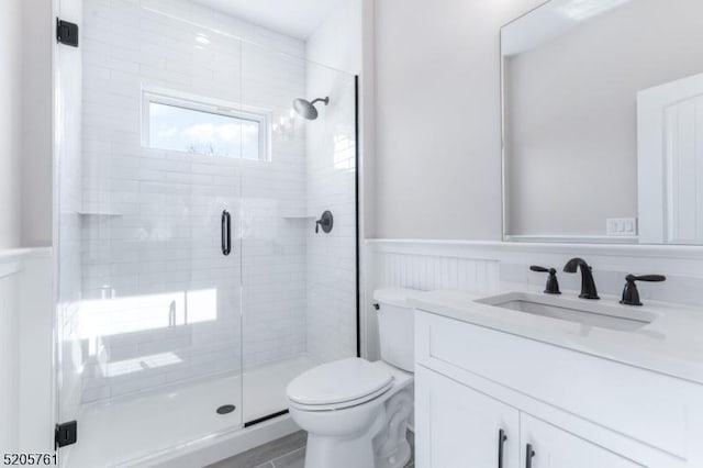 bathroom with a wainscoted wall, a stall shower, vanity, and toilet