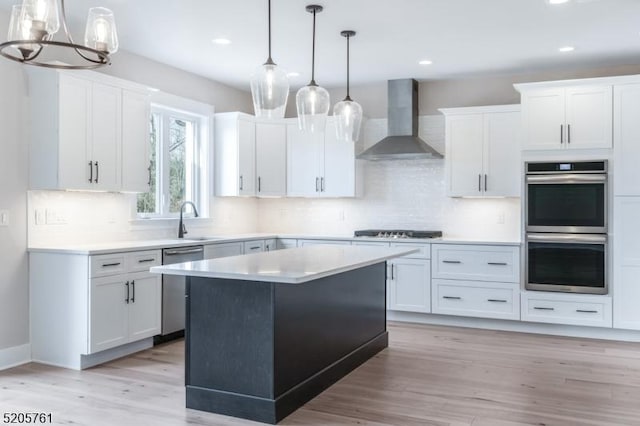 kitchen with appliances with stainless steel finishes, white cabinets, a sink, light wood-type flooring, and wall chimney exhaust hood